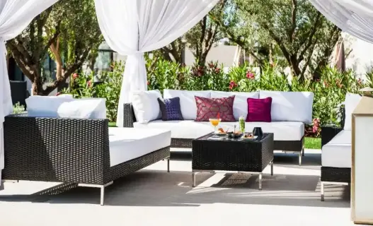 Elegante Lounge-Sitzgelegenheiten im Freien mit weißen Kissen, geflochtenen Möbeln und Gartenumgebung im STORY Rabat, einem 5-Sterne-Hotel in Rabat, Marokko.