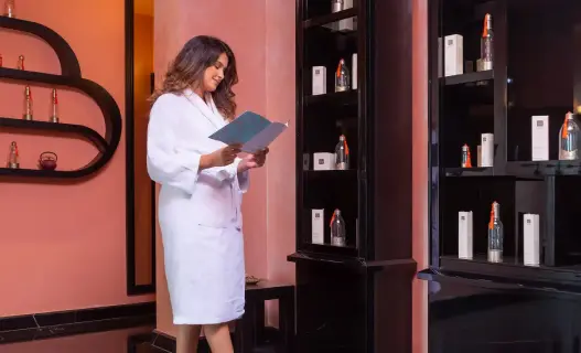 Frau in weißem Bademantel, die in einem luxuriösen Spa-Bereich des STORY Rabat, einem der Luxushotels in Marokko, eine Behandlungskarte liest.