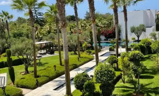 Üppiger grüner Garten mit Palmen, angelegten Wegen und Schwimmbadbereich im STORY Rabat, einem luxuriösen 5-Sterne-Hotel in Rabat, Marokko.