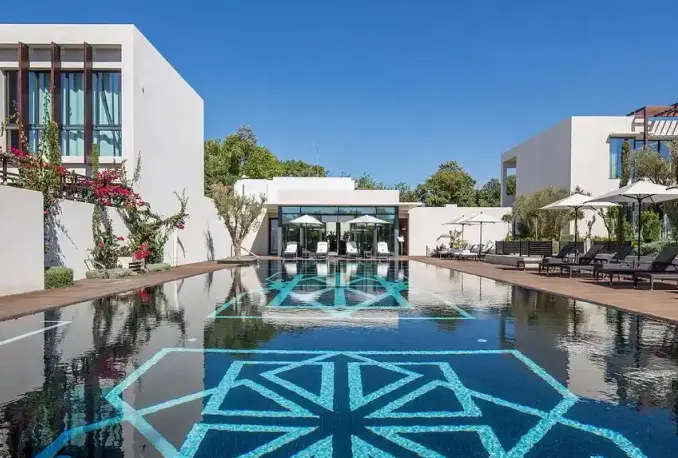 La magnifique piscine extérieure du STORY Rabat, ornée de mosaïques bleues complexes, est entourée de chaises longues et de parasols. Elle est idéale pour se détendre et profiter du beau temps dans l'un des meilleurs hôtels de luxe de Rabat, au Maroc.