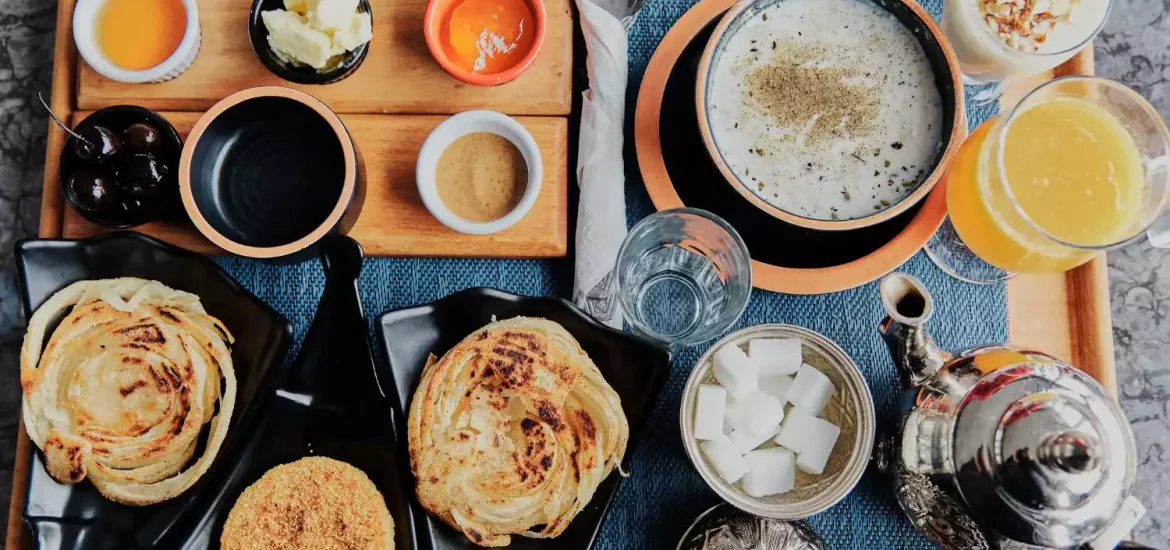 Traditional Moroccan breakfast spread featuring msemen, olive oil, sugar cubes, and mint tea served with local breads and fresh orange juice.
