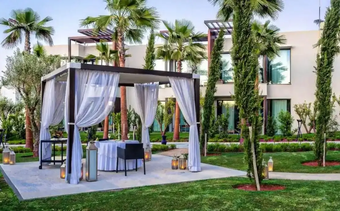 Un dîner romantique en plein air à STORY Rabat avec une pergola entourée de verdure luxuriante, comprenant une table pour deux, des rideaux élégamment drapés et des lanternes, parfait pour un dîner privé et luxueux à Rabat, au Maroc.