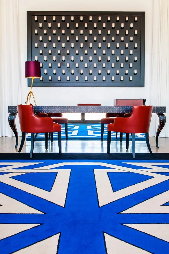 Moderner Hotel-Loungebereich mit roten Sesseln, blauem geometrischem Teppich, dekorativer Wandkunst und eleganter Beleuchtung in einem Luxushotel in Rabat, Marokko.