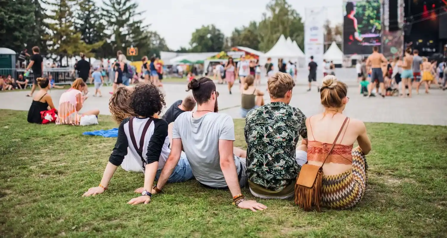 Groupe d'amis se détendant sur l'herbe entre deux concerts lors d'un festival de musique en plein air.