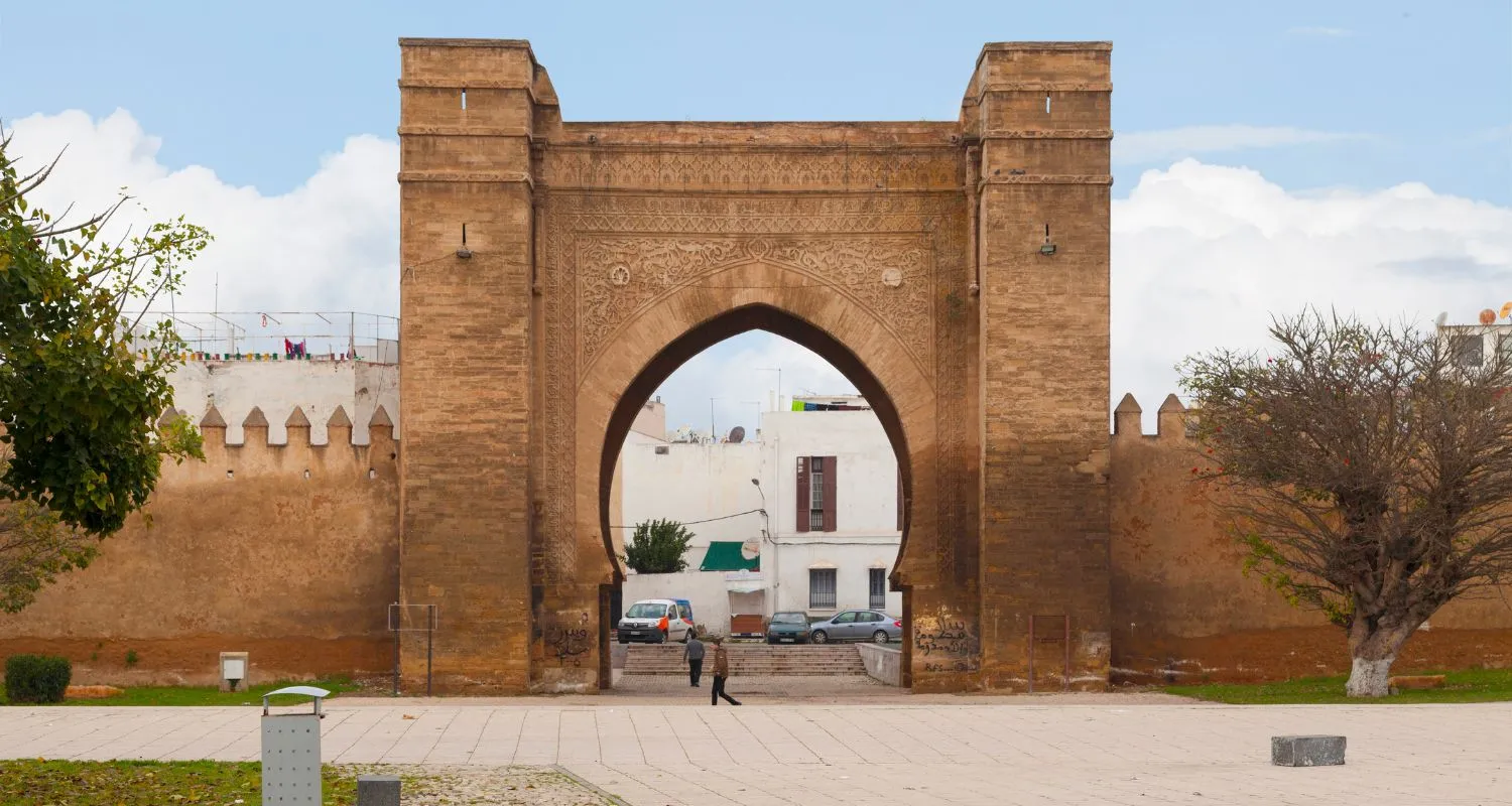 Bab Mrisa, the monumental horseshoe-arch stone gate in the walls of Salé medina, with crenellated ramparts and people crossing the square