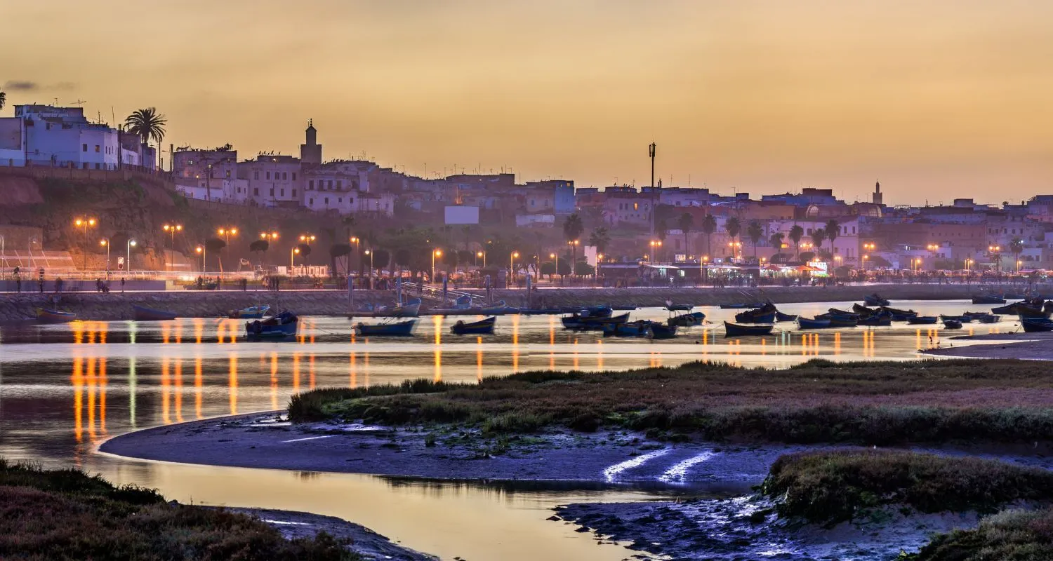 Sunset over the Bou Regreg river separating Salé medina and Rabat, with fishing boats moored along the water and marshland in the foreground