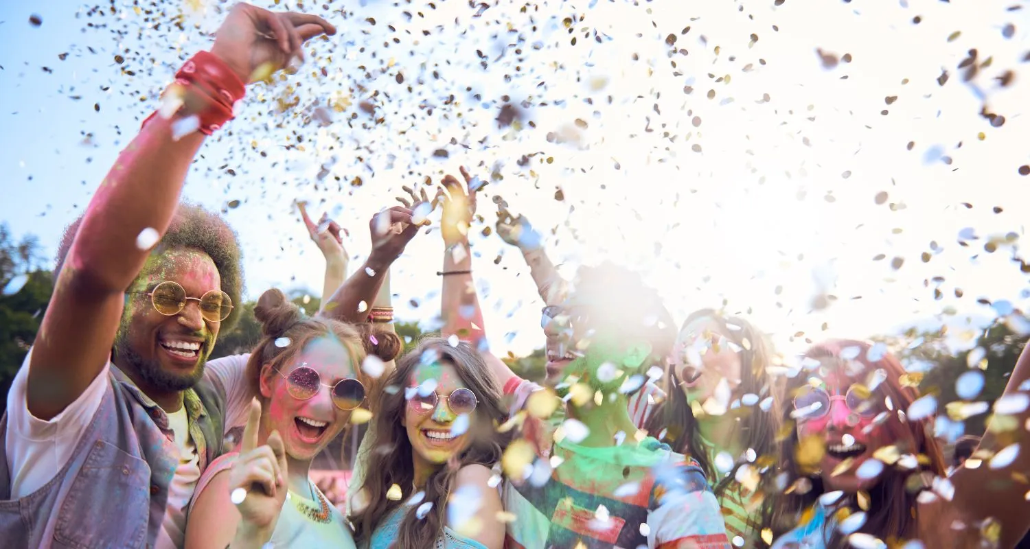 Friends celebrating at an outdoor festival with confetti and colorful powder