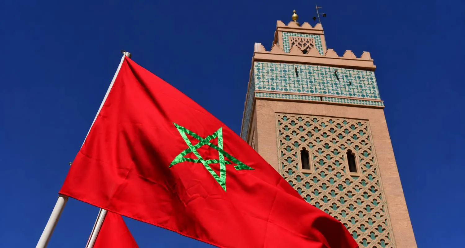 Moroccan flag flying beside a tiled minaret under a clear blue sky